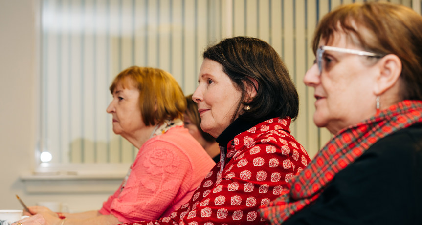 Three women sitting side-by-side at a meeting table.