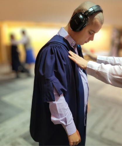 A young man getting ready for his graduation. You can see a person's hands smoothing his graduation robes.